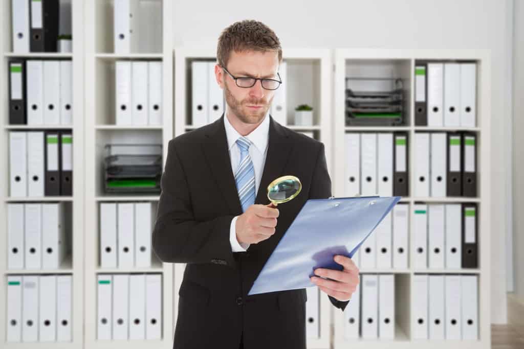 Private security investigator looking at document through magnifying glass in office