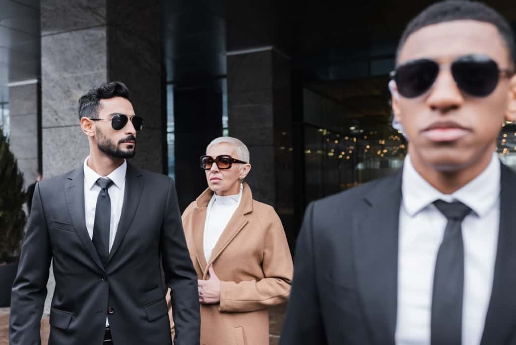 Multi-racial bodyguards protecting a mature high-net-worth female person existing a building